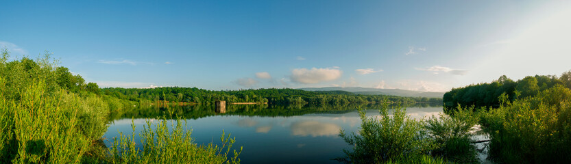 Obraz premium Panoramic landscape from the lake with colorful clouds in the summer sun.