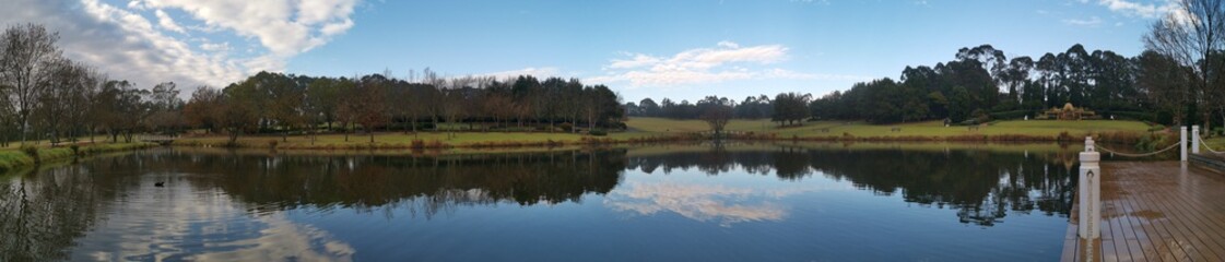 Beautiful morning panoramic view of a still pond in a park with stunning reflections of blue puffy sky and tall trees, Fagan park, Galston, Sydney, New South Wales, Australia