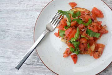 Bruschetta, Italian appetizer of toasted bread with garlic and olive oil, served with diced tomatoes and basil on a plate and a grey table with copy space, high angle view from above, selected focus