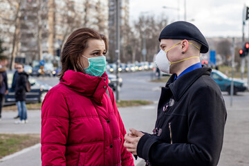 Young couple wearing two types of protective masks for protection from coronavirus, smog or other atmospheric pollutants in big city. Conceptual photo about ecology and Covid 19 outbreak (pandemic).