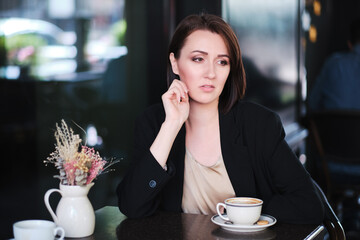 pensive or thoughtful woman sitting at table in cafe wearing black jacket - 367621056