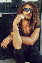 Handsome man with curly hair and jewelry on his arms and chest, outdoor photoshoot under the sun - image - 367622230