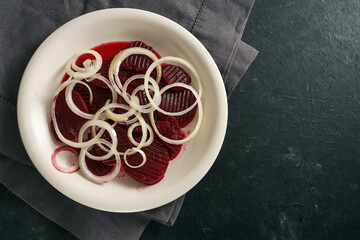 Beetroot slices with onion rings, healthy salad on a white plate and a gray napkin on a dark slate background, copy space, high angle view from above