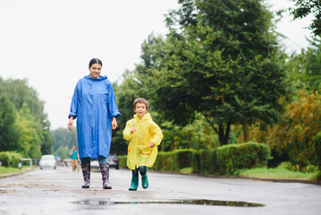 Fototapeta premium Mom and son in raincoats have fun together in the rain. concept of family vacation and happy childhood.