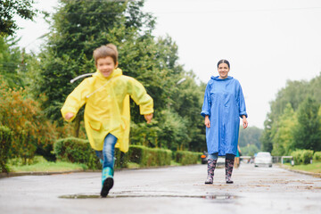 Fototapeta premium Mother and child, boy, playing in the rain, wearing boots and raincoats