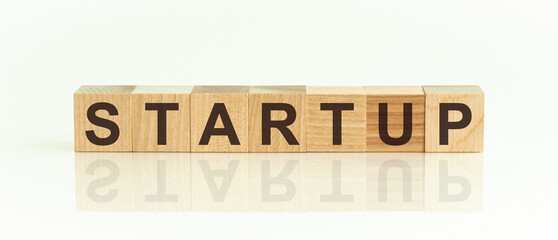 Wooden Blocks with the text: sturtupt. The text is written in black letters and is reflected in the mirror surface of the table. New business relaunch startup concept.