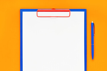 Blank clipboard mockup and blue pen on orange color background. Top view, copy space. Back to school, deadline, morning concept.