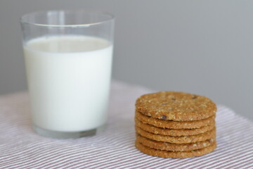Oat cookies with glass of milk for breakfast on table cloth and blue flower on background, rustic healthy food 