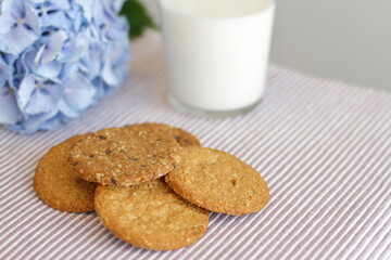 Oat cookies with glass of milk for breakfast on table cloth and blue flower on background, rustic healthy food 