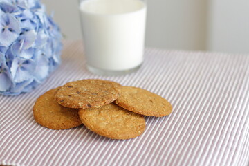Fototapeta na wymiar Oat cookies with glass of milk for breakfast on table cloth and blue flower on background, rustic healthy food 