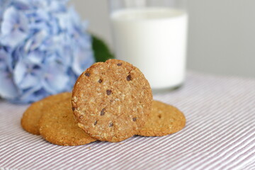 Oat cookies with glass of milk for breakfast on table cloth and blue flower on background, rustic healthy food 