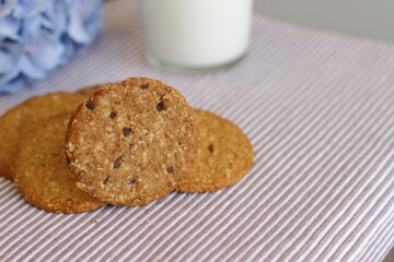 Oat cookies with glass of milk for breakfast on table cloth and blue flower on background, rustic healthy food 