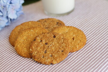 Oat cookies with glass of milk for breakfast on table cloth and blue flower on background, rustic healthy food 