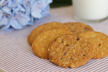 Oat cookies with glass of milk for breakfast on table cloth and blue flower on background, rustic healthy food 