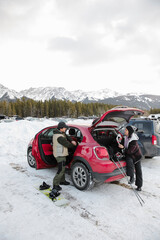 Couple unloading snowboarding and ski equipment in snowy parking lot