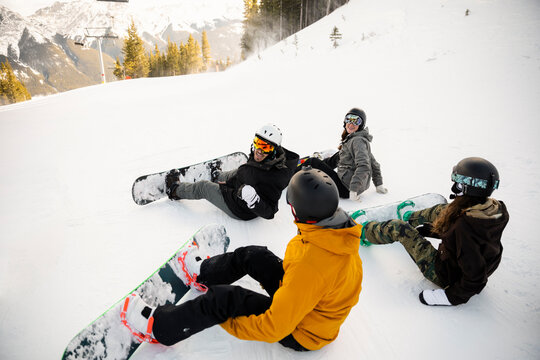 Snowboarder friends sitting in snow on mountain ski slope