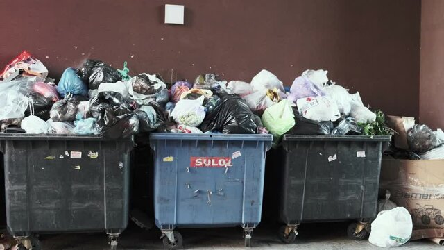Overflowing trash cans on the street along the wall. Unsorted waste concept, harm to the environment