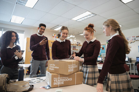 Excited high school students opening yearbook boxes in classroom