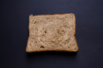A slice of wholemeal bread on a black background.