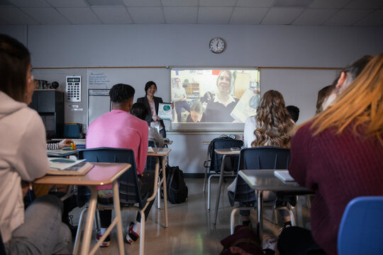 High school students watching video on projection screen in classroom