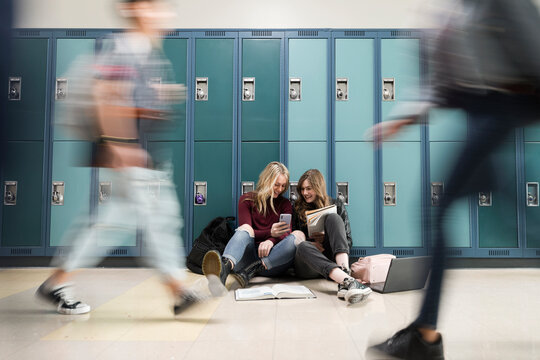High school girl friends using smart phone at lockers in corridor