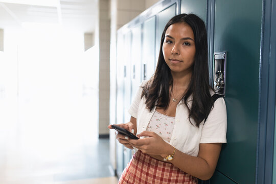 Portrait confident high school girl using smart phone at lockers in corridor