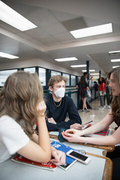 High school boy student in flu mask talking with friends in corridor