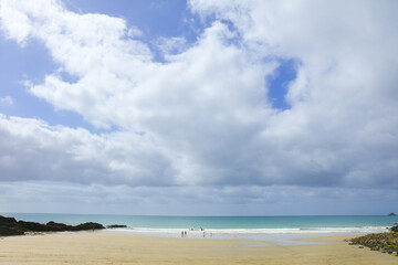 Cornwall beach on Porthluney Bay with cloudy blue sky and horizon over the water
