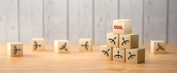 cubes with bow and arrow symbols pointing all to the top to the message GOAL in front of wooden background