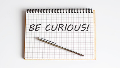 BE CURIOUS! text written on a notebook with pen