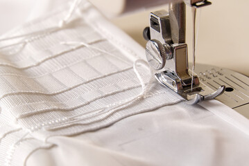 A worker works on a sewing machine. seamstress sews white curtains, close up view.
