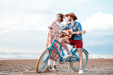 Young couple, looking at the sunset and smiling. Boy is holding the guitar