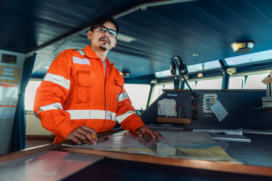 Filipino deck Officer on bridge of vessel or ship wearing coverall during navigaton watch at sea . He is plotting position on chart
