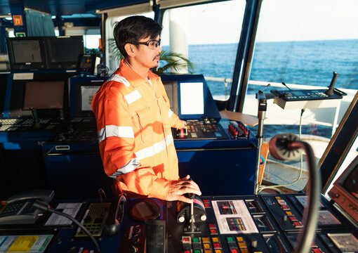 Filipino deck Officer on bridge of vessel or ship wearing coverall during navigaton watch at sea . He is maneuvering with cpp thrusters propulsion
