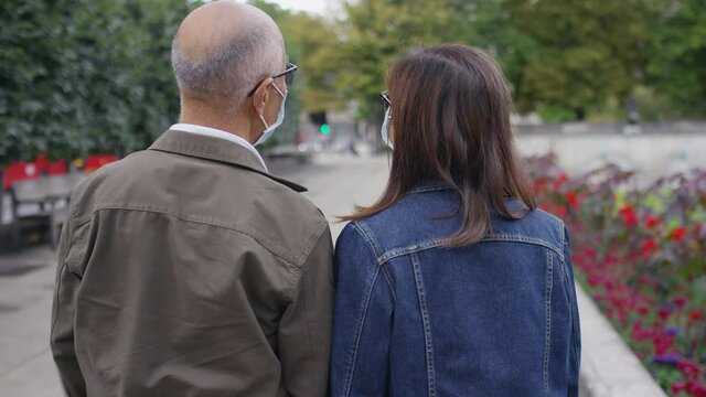 Camera follows a senior Chinese couple wearing face masks as they walk through a quiet city, in slow motion