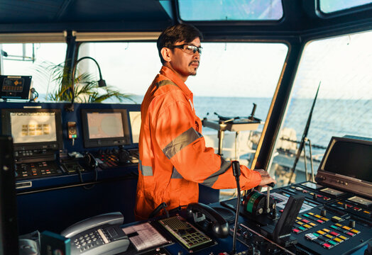 Filipino deck Officer on bridge of vessel or ship wearing coverall during navigaton watch at sea . He is maneuvering with cpp thrusters propulsion
