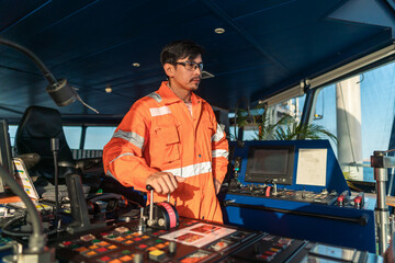 Filipino deck Officer on bridge of vessel or ship wearing coverall during navigaton watch at sea . He is maneuvering with cpp thrusters propulsion