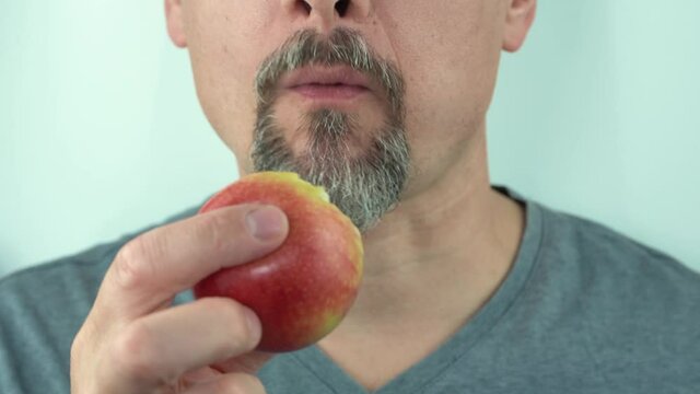 A man of middle ages with beard and mustache eating a red apple, close-up, 4K