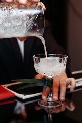 hands of a bartender holding a shaker pouring a drink into a glass