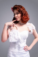 Cute and Positive Smiling Redhaired Caucasian Female Posing in White Wedding Dress and Little Purse Against Gray Background.