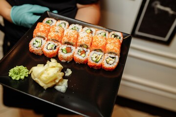 Hand Waiter holding Set Delicious fresh Sushi slate plate, Japanese raw fish in traditional restaurant. Philadelphia fresh Rolls served on plate in sushi bar. waiter in gloves holds sushi rolls