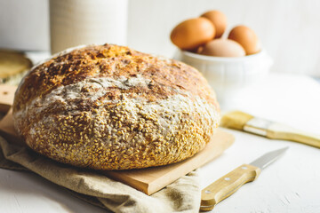 Homemade sourdough bread, some eggs, oil, sesame, wood cutting board, white background, wood knife and napkin.