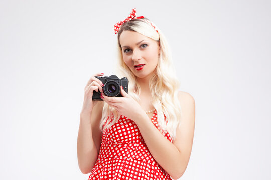 Pin-up Girl Concepts. Caucasian Blond Girl Posing in Pin-up Style and Holding Retro Film Camera in Hands. Against White.