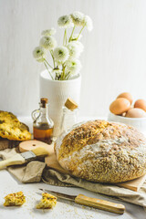 Homemade sourdough bread, some eggs, oil, sesame, wood cutting board, white background, wood knife and napkin.