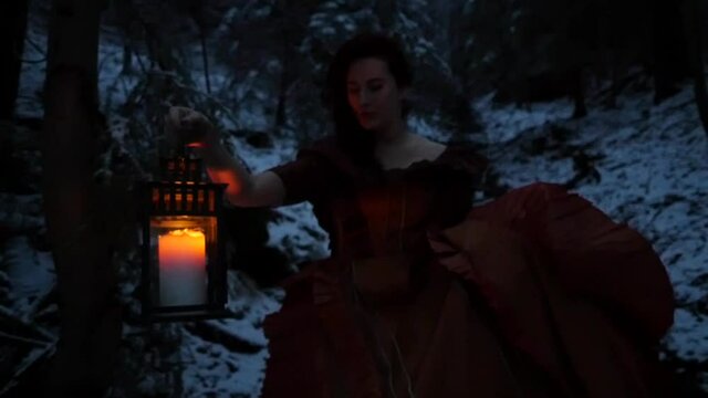 Woman holding a lantern walking in the forest in the winter at Dawn. Wearing a ball dress. Slow Motion