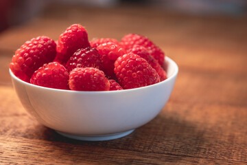 Fototapeta na wymiar Close up shot of a white bowl of raspberries on a weathered, rustic, brown wooden table with a blurred background