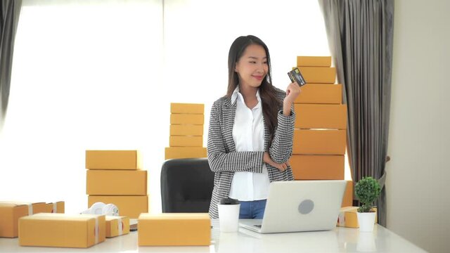 A young successful businesswoman surround by boxes waiting to be shipped hold up her credit card in triumph.