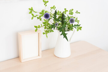 小さな白い花瓶の花と写真立て　木製　木目　フォトフレーム　花瓶　白　ナチュラル　緑　植物　花　葉　自然　観葉植物　部屋　室内　空間　背景　余白　ホワイトスペース　文字スペース　コピースペース