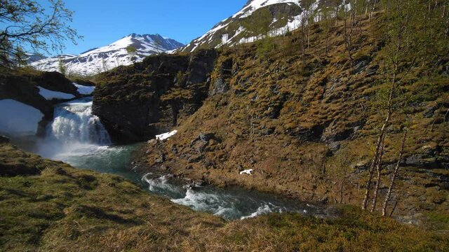 Static view of a waterfall with snowy mountain in the background, on a sunny, summer day, in the Lyngen alps, North Norway