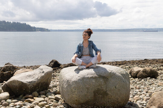 Young woman sitting on a large rock with the ocean behind